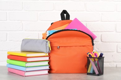 Photo of Backpack with different school stationery on light grey table near brick wall