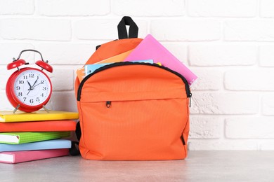 Photo of Backpack with different school stationery and alarm clock on light grey table near brick wall. Space for text