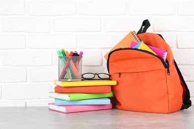 Photo of Backpack with different school stationery on light grey table near brick wall