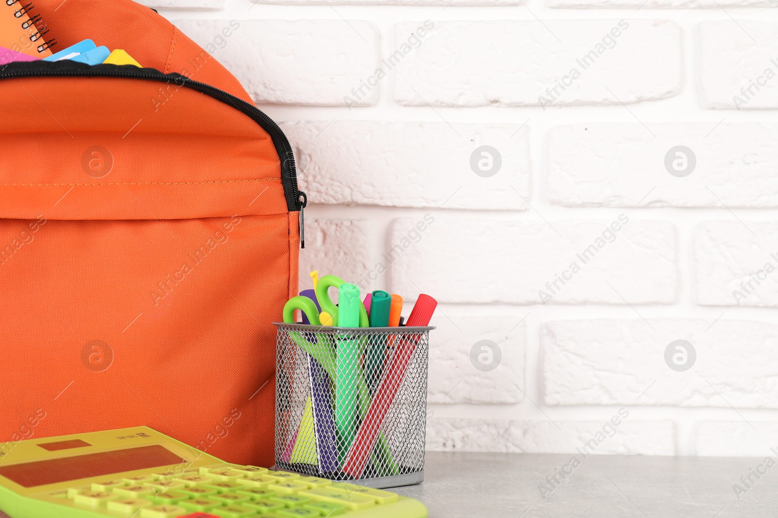 Photo of Backpack with different school stationery on light grey table near brick wall, closeup. Space for text