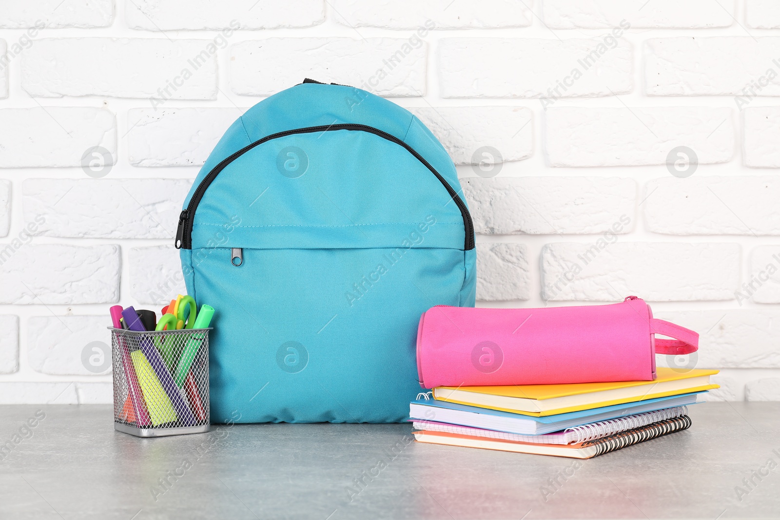 Photo of Backpack with different school stationery on light grey table near brick wall