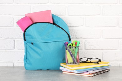 Photo of Backpack with different school stationery on light grey table near brick wall