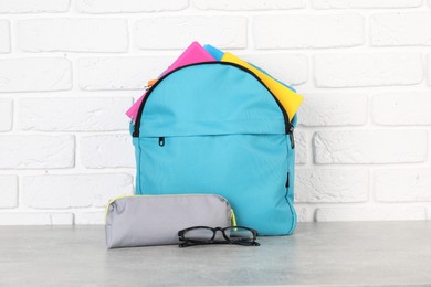 Photo of Backpack with different school stationery on light grey table near brick wall