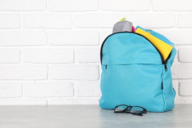 Photo of Backpack with different school stationery on light grey table near brick wall. Space for text