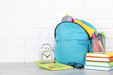 Photo of Backpack with different school stationery and alarm clock on light grey table near brick wall. Space for text