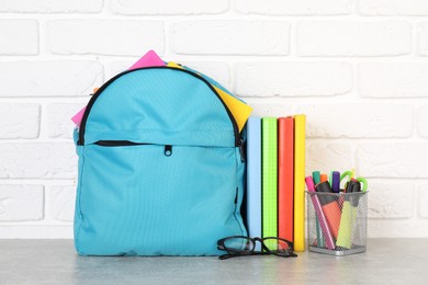 Photo of Backpack with different school stationery on light grey table near brick wall