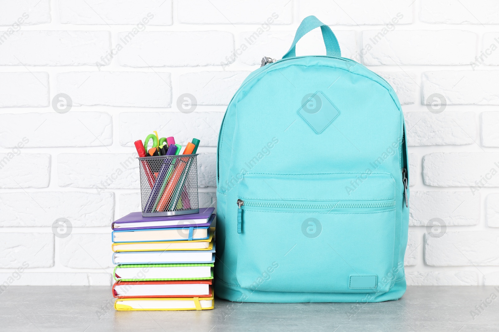 Photo of Backpack with different school stationery on light grey table near brick wall