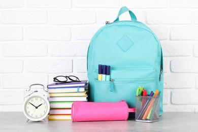 Photo of Backpack with different school stationery and alarm clock on light grey table near brick wall