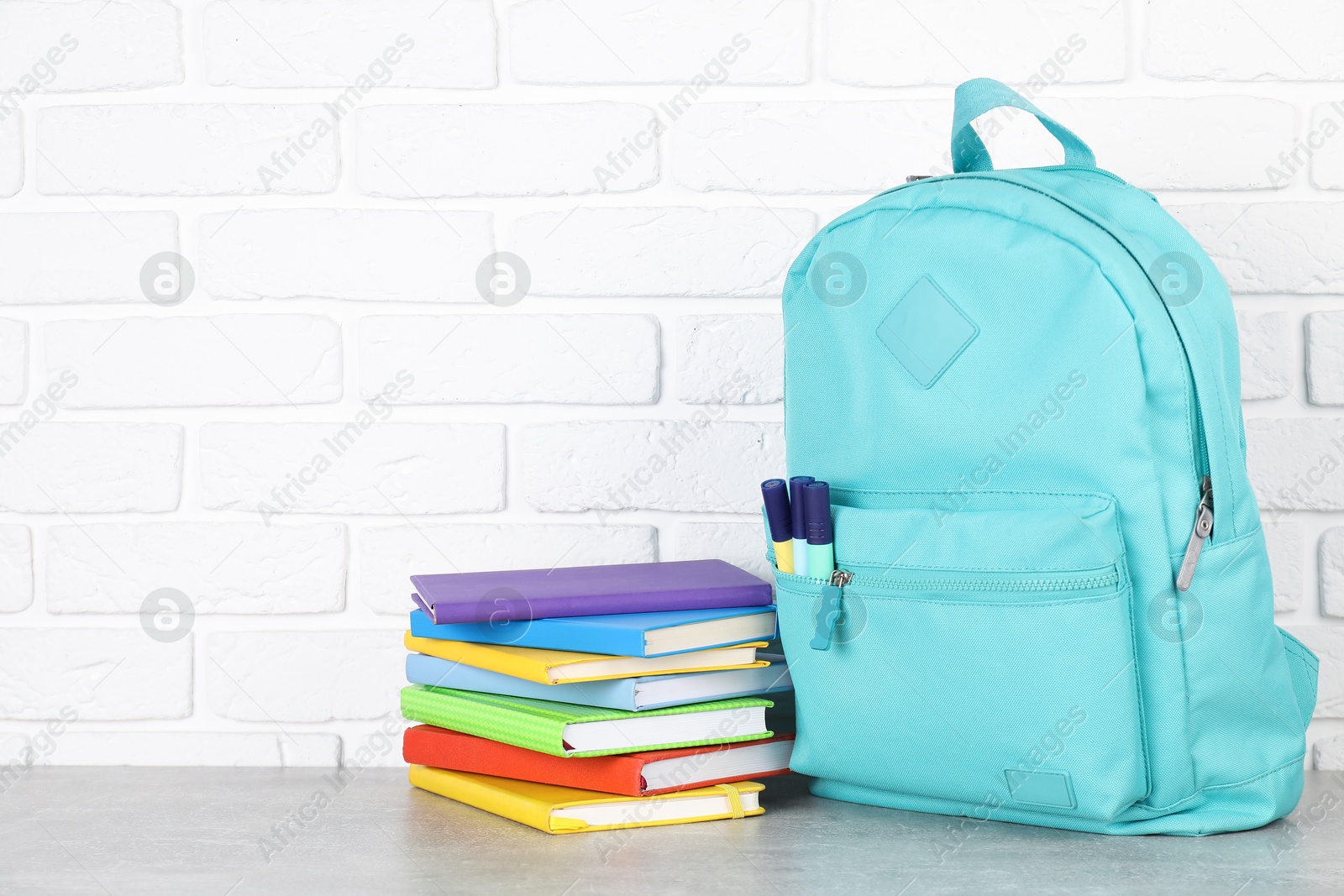 Photo of Backpack with different school stationery on light grey table near brick wall. Space for text