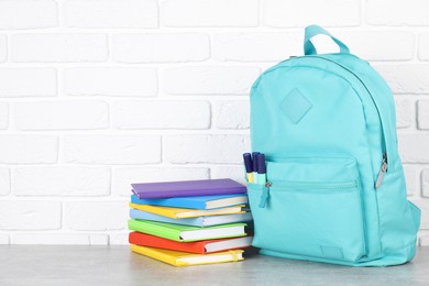 Photo of Backpack with different school stationery on light grey table near brick wall. Space for text