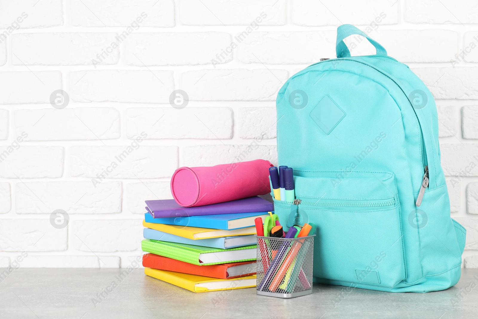 Photo of Backpack with different school stationery on light grey table near brick wall. Space for text