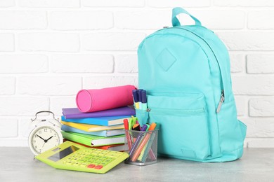 Photo of Backpack with different school stationery and alarm clock on light grey table near brick wall