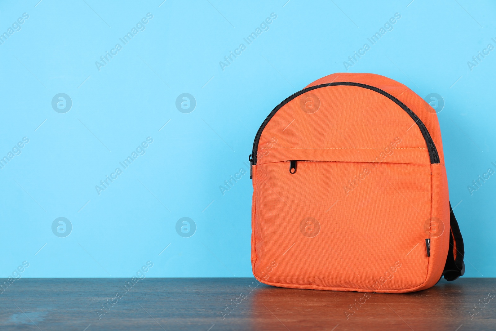 Photo of Orange backpack on wooden table against light blue background. Space for text