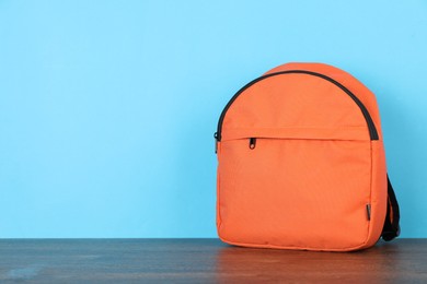 Photo of Orange backpack on wooden table against light blue background. Space for text