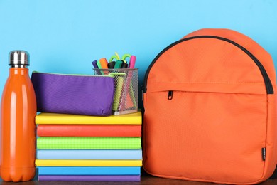 Photo of Backpack with different school stationery and bottle on wooden table against light blue background