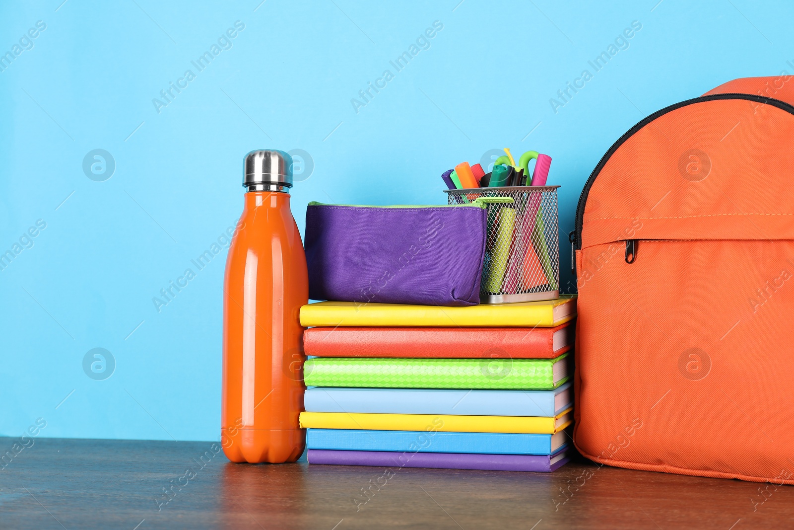 Photo of Backpack with different school stationery and bottle on wooden table against light blue background