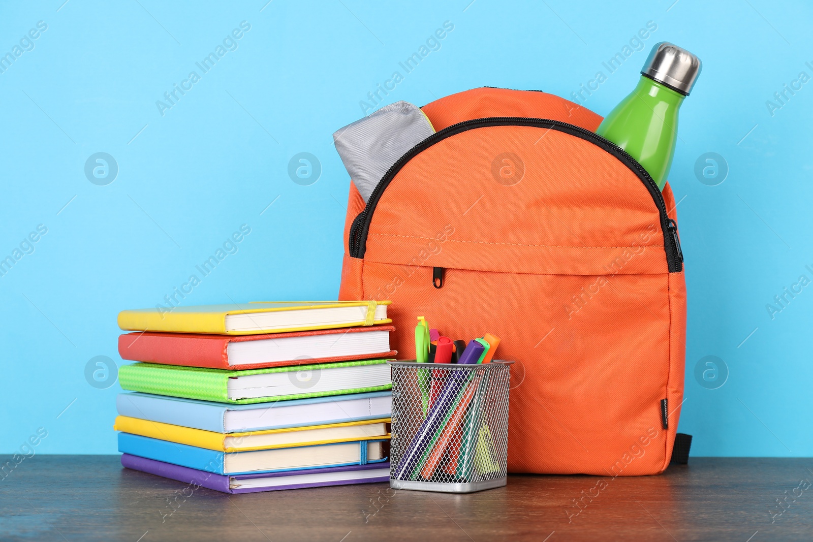 Photo of Backpack with different school stationery on wooden table against light blue background