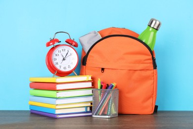 Photo of Backpack with different school stationery and alarm clock on wooden table against light blue background