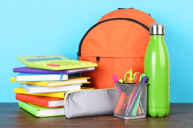 Photo of Backpack with different school stationery on wooden table against light blue background