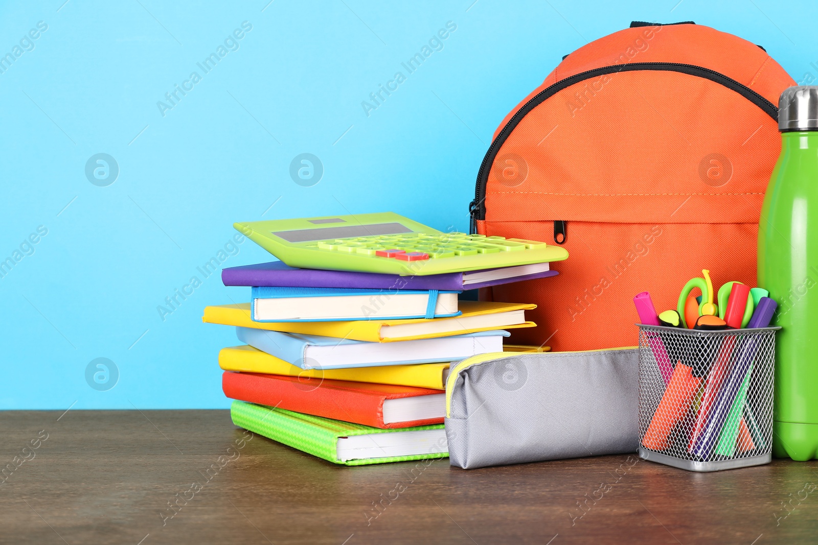 Photo of Backpack with different school stationery on wooden table against light blue background