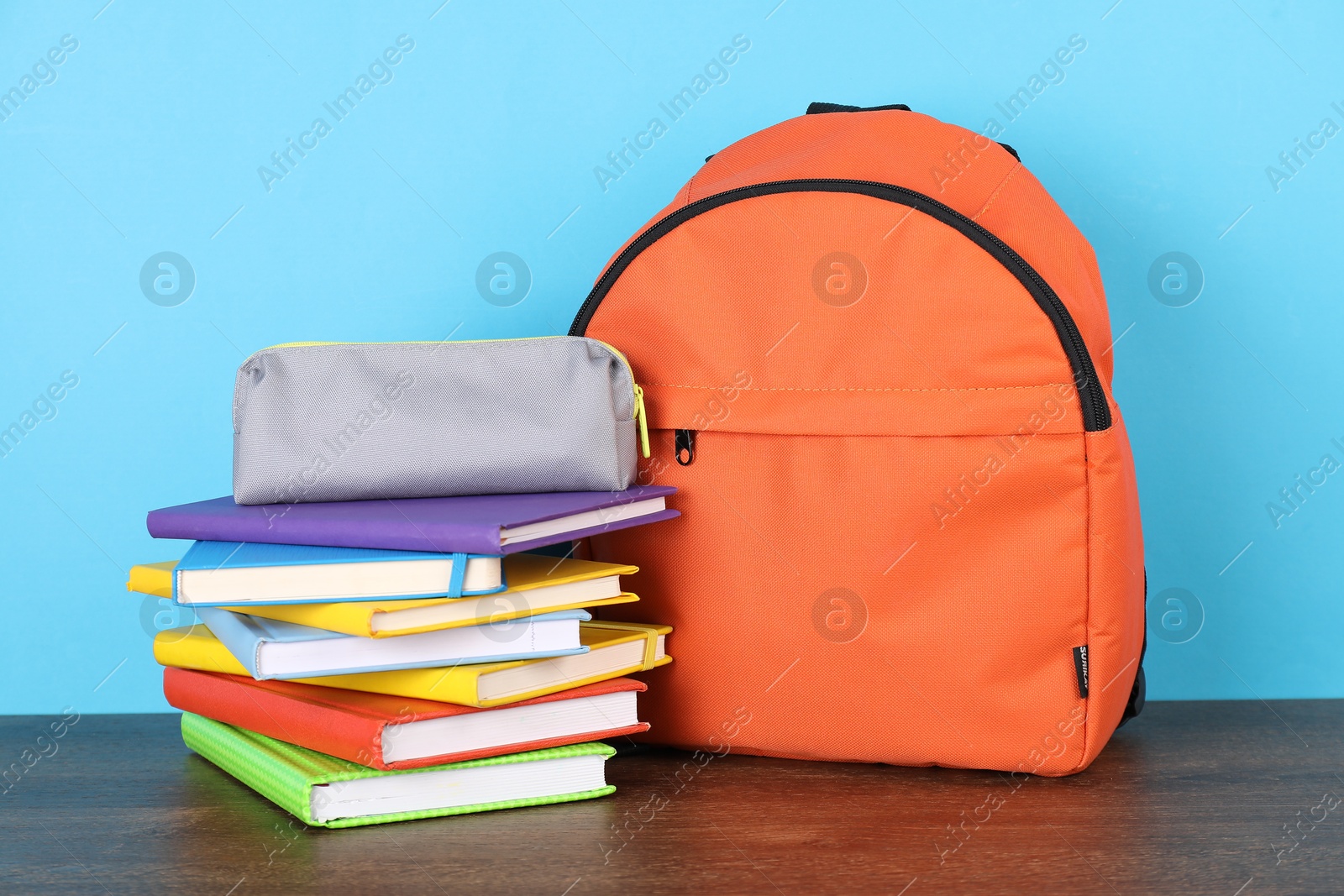 Photo of Backpack with different school stationery on wooden table against light blue background