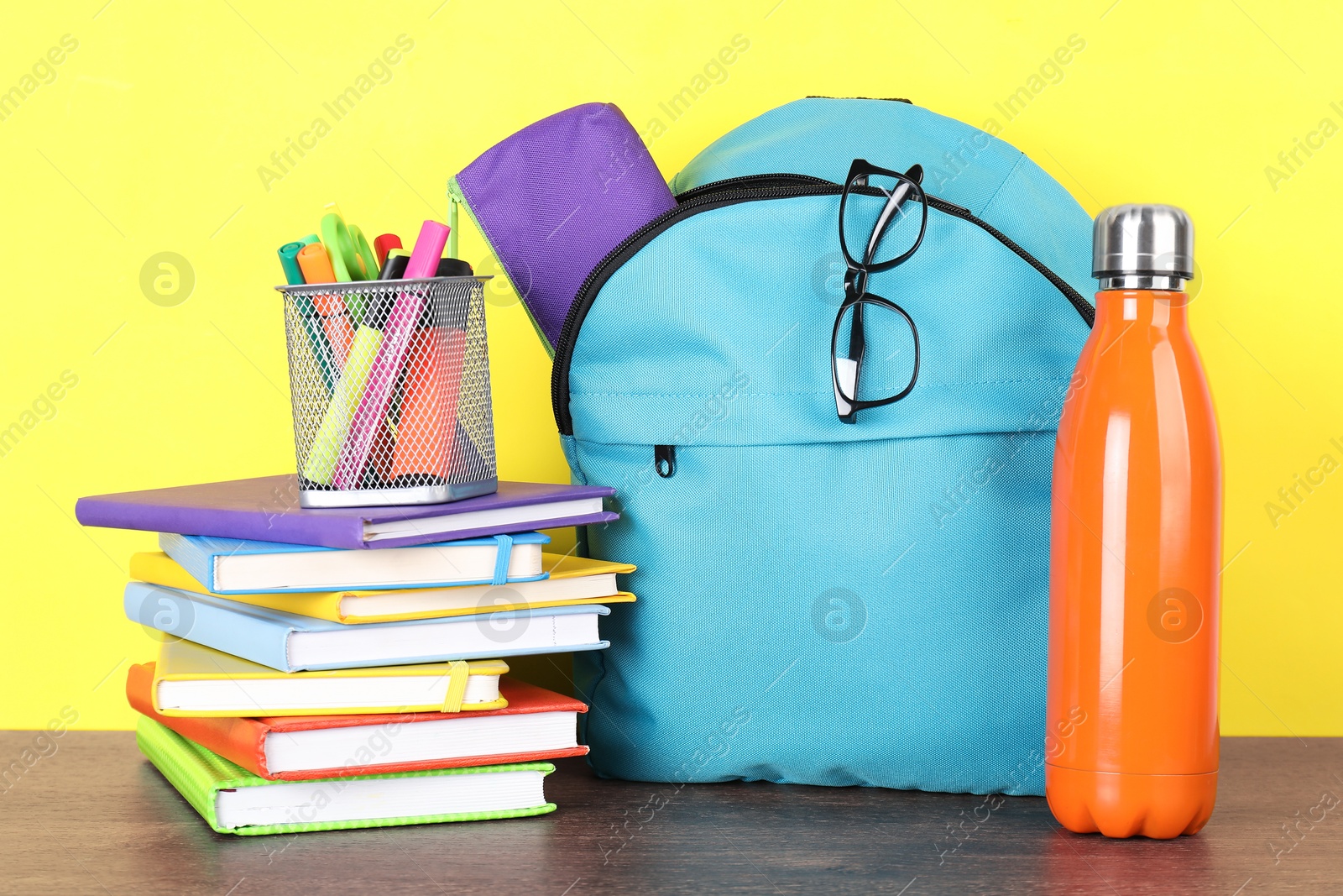 Photo of Backpack with different school stationery and bottle on wooden table against yellow background