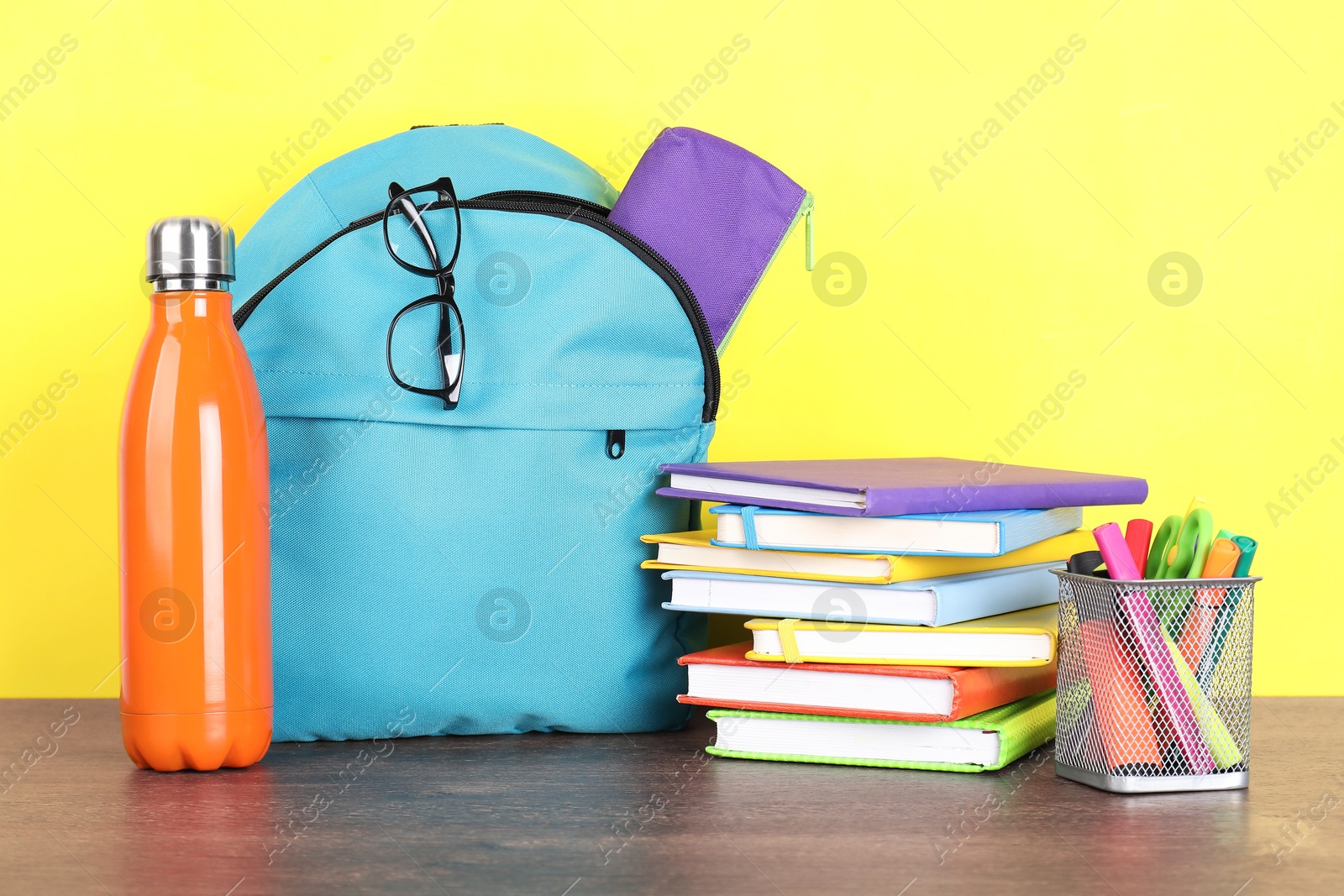 Photo of Backpack with different school stationery and bottle on wooden table against yellow background