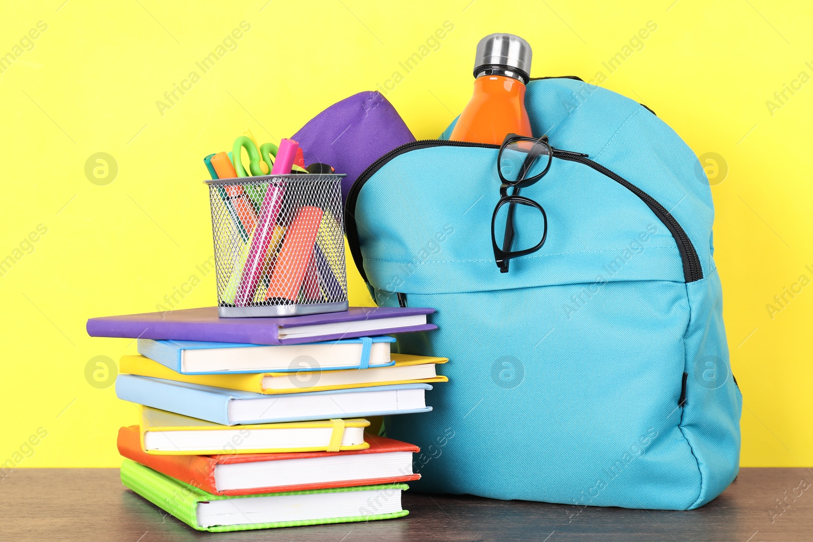 Photo of Backpack with different school stationery and bottle on wooden table against yellow background