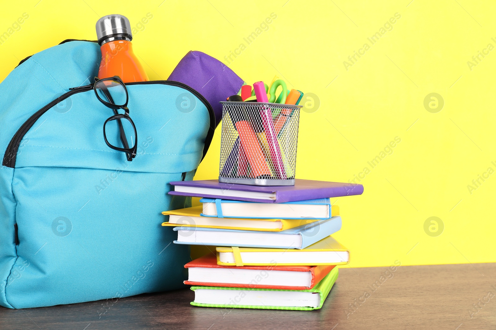 Photo of Backpack with different school stationery and bottle on wooden table against yellow background