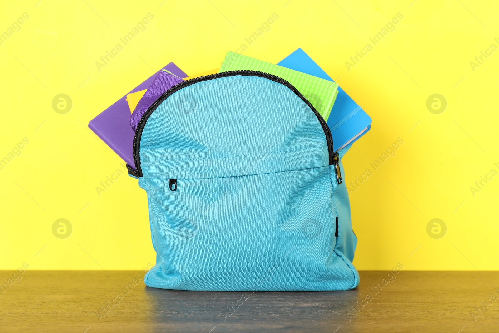 Photo of Backpack with different school stationery on wooden table against yellow background