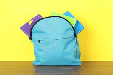 Photo of Backpack with different school stationery on wooden table against yellow background