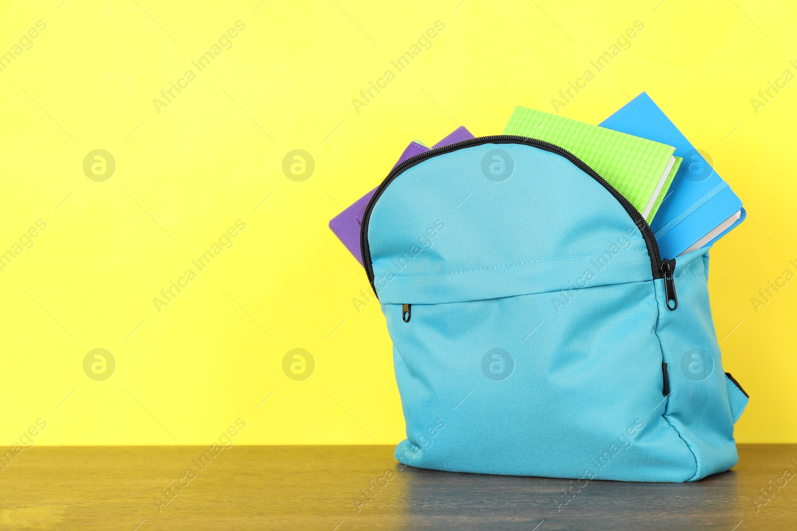 Photo of Backpack with different school stationery on wooden table against yellow background. Space for text