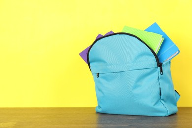 Photo of Backpack with different school stationery on wooden table against yellow background. Space for text