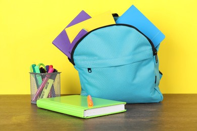 Photo of Backpack with different school stationery on wooden table against yellow background