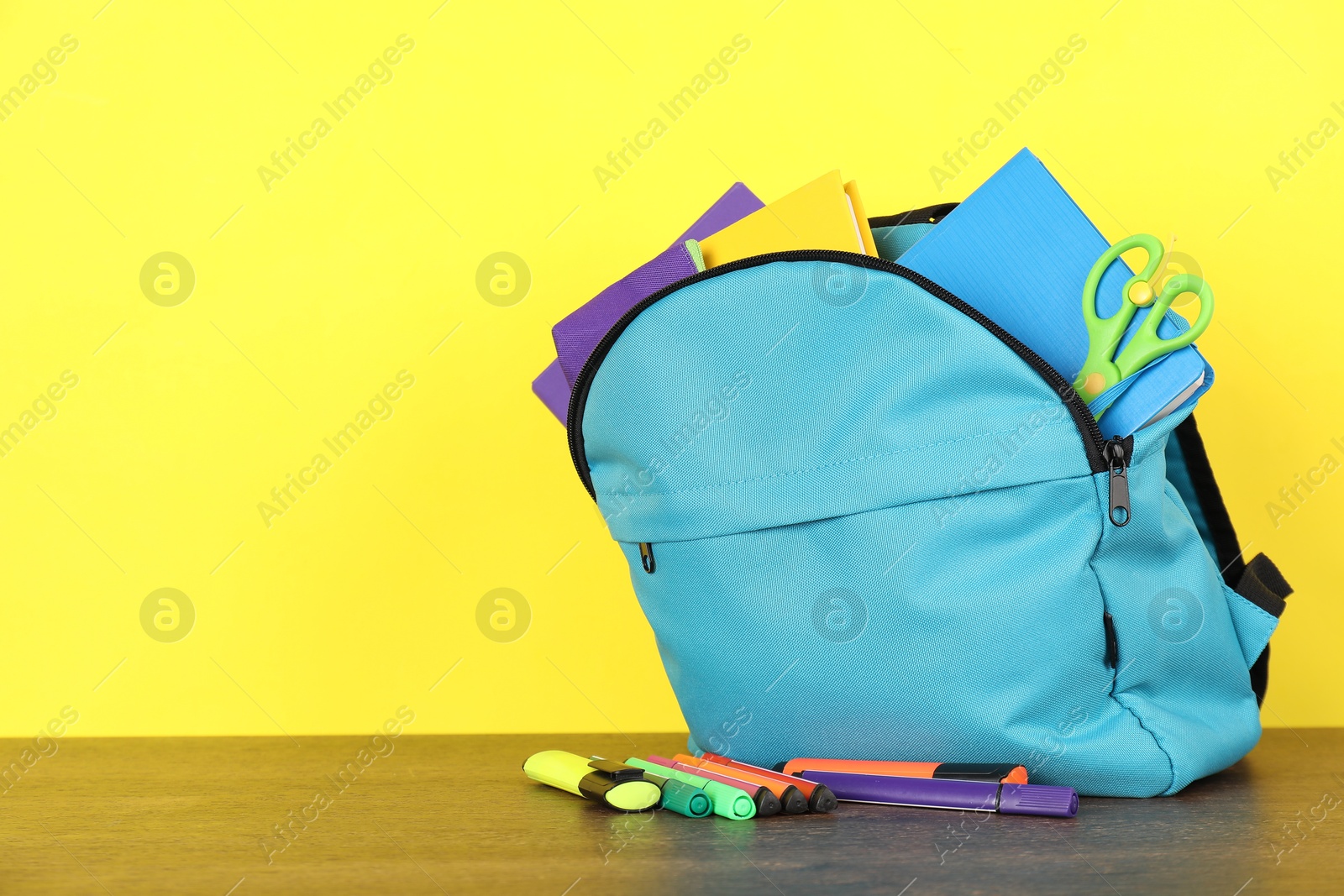 Photo of Backpack with different school stationery on wooden table against yellow background