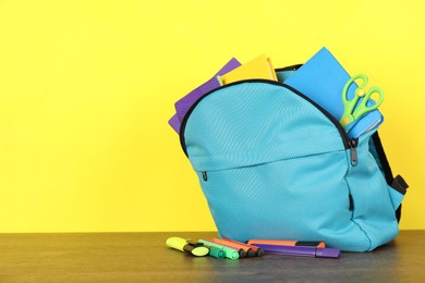 Photo of Backpack with different school stationery on wooden table against yellow background