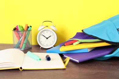 Photo of Backpack with different school stationery and alarm clock on wooden table against yellow background