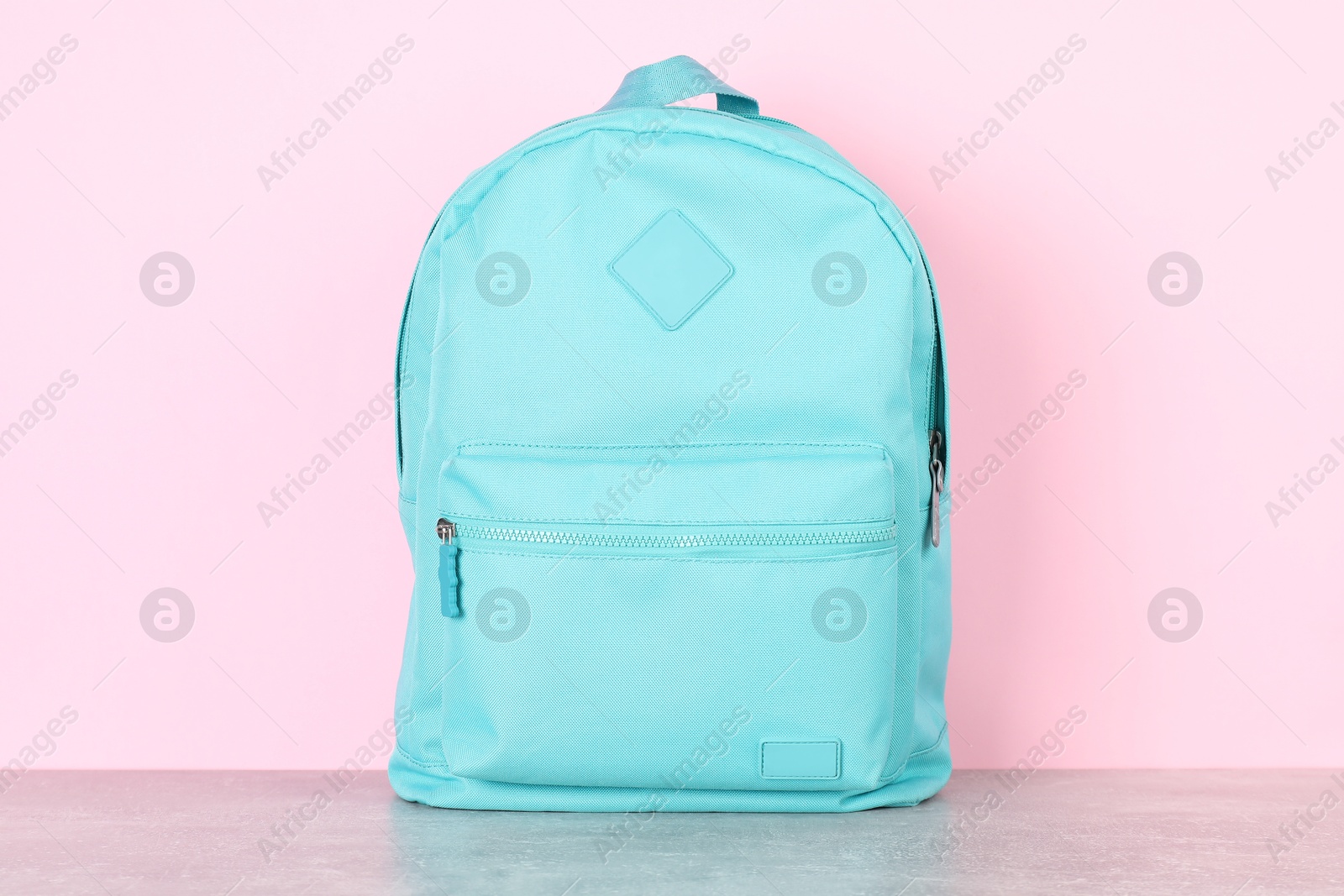 Photo of Light blue backpack on grey table against pink background