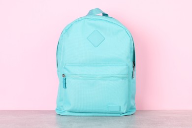 Light blue backpack on grey table against pink background