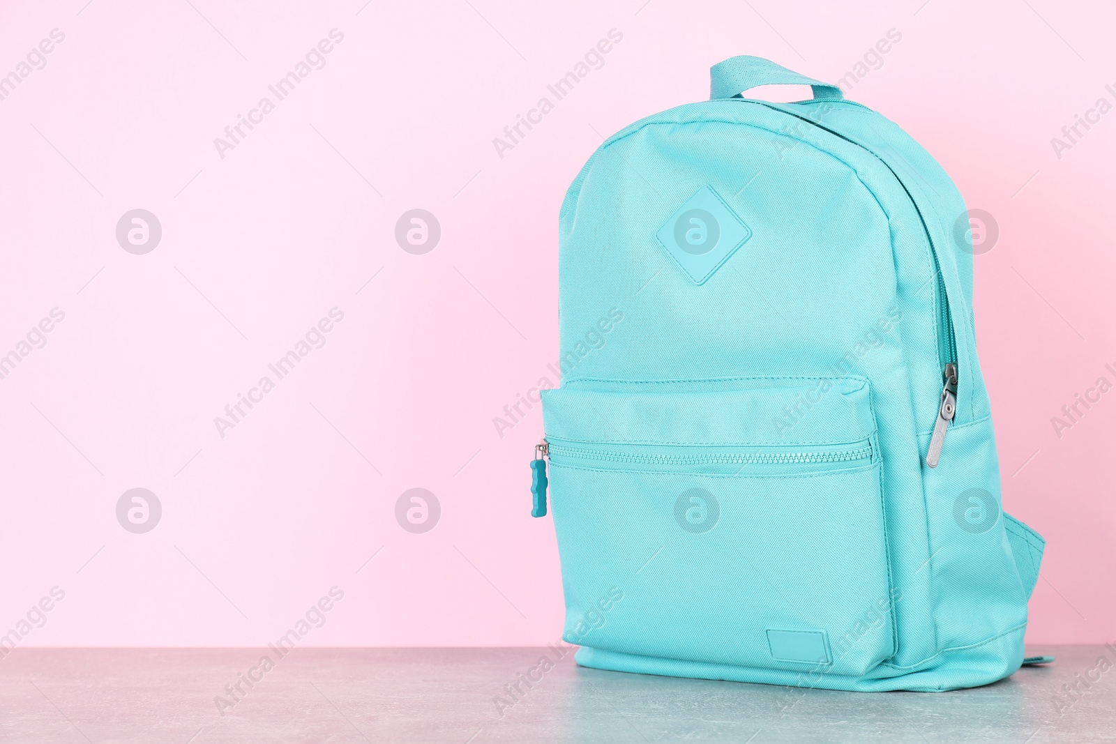 Photo of Light blue backpack on grey table against pink background. Space for text