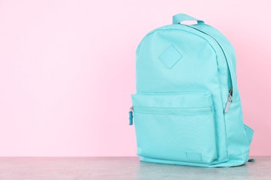 Photo of Light blue backpack on grey table against pink background. Space for text