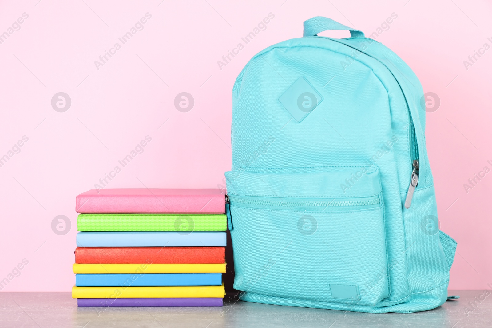 Photo of Backpack with different school stationery on light grey table against pink background