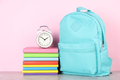 Photo of Backpack with different school stationery and alarm clock on light grey table against pink background