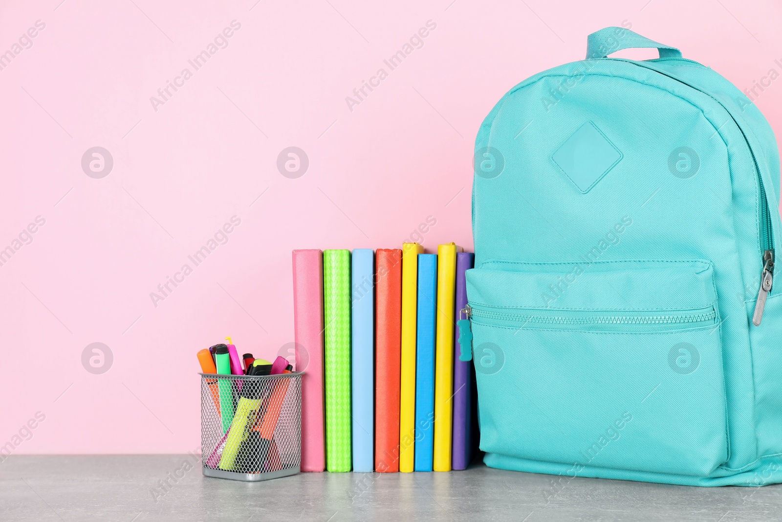 Photo of Backpack with different school stationery on light grey table against pink background