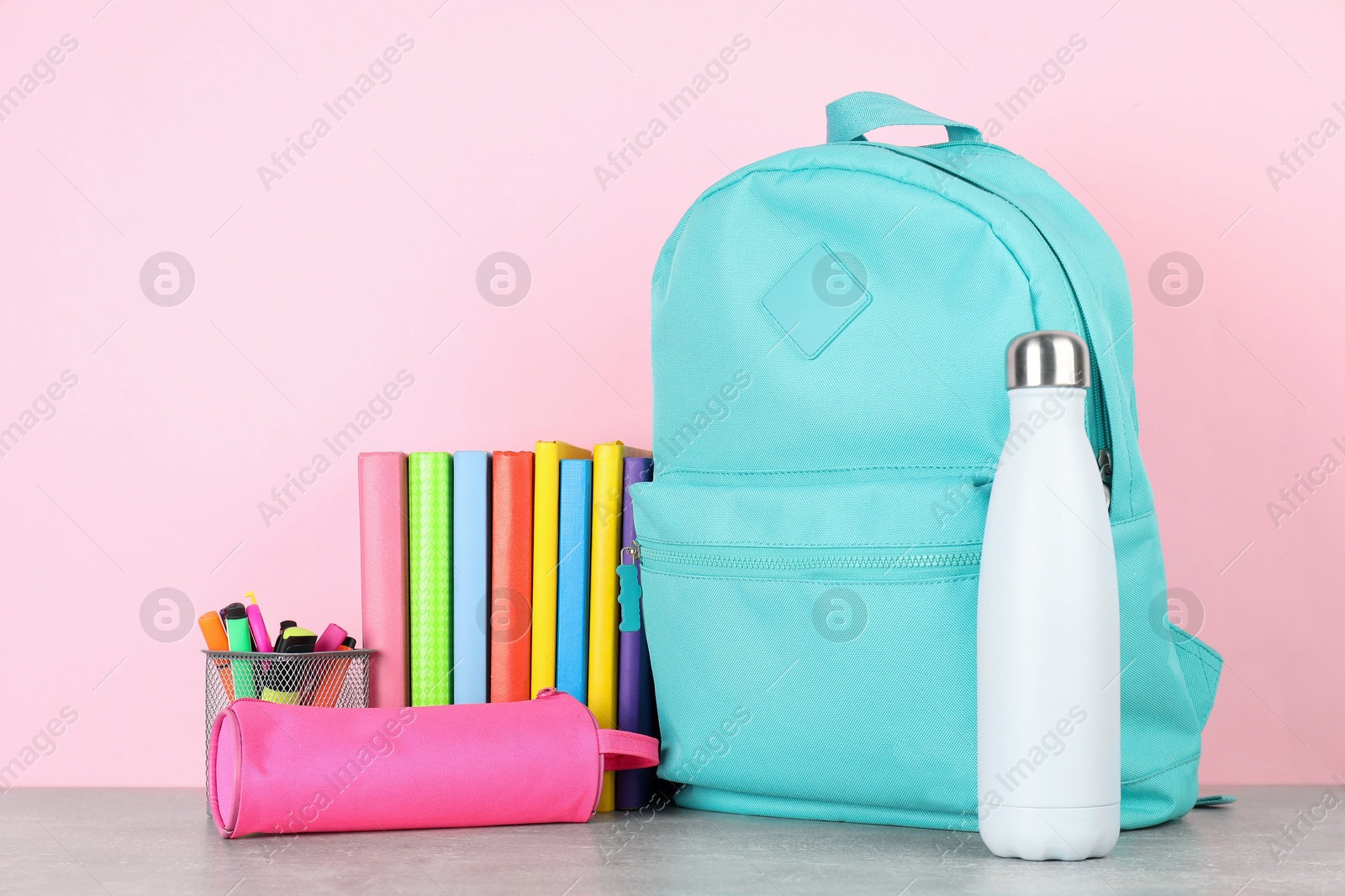 Photo of Backpack with different school stationery and bottle on light grey table against pink background