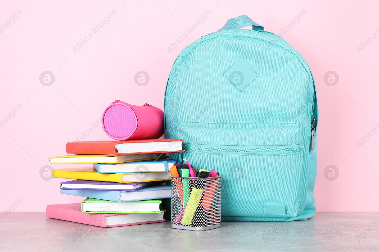 Photo of Backpack with different school stationery on light grey table against pink background