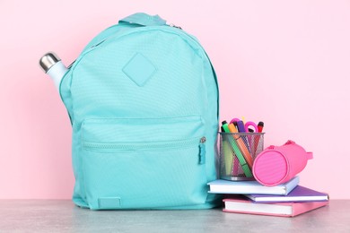 Photo of Backpack with different school stationery on light grey table against pink background