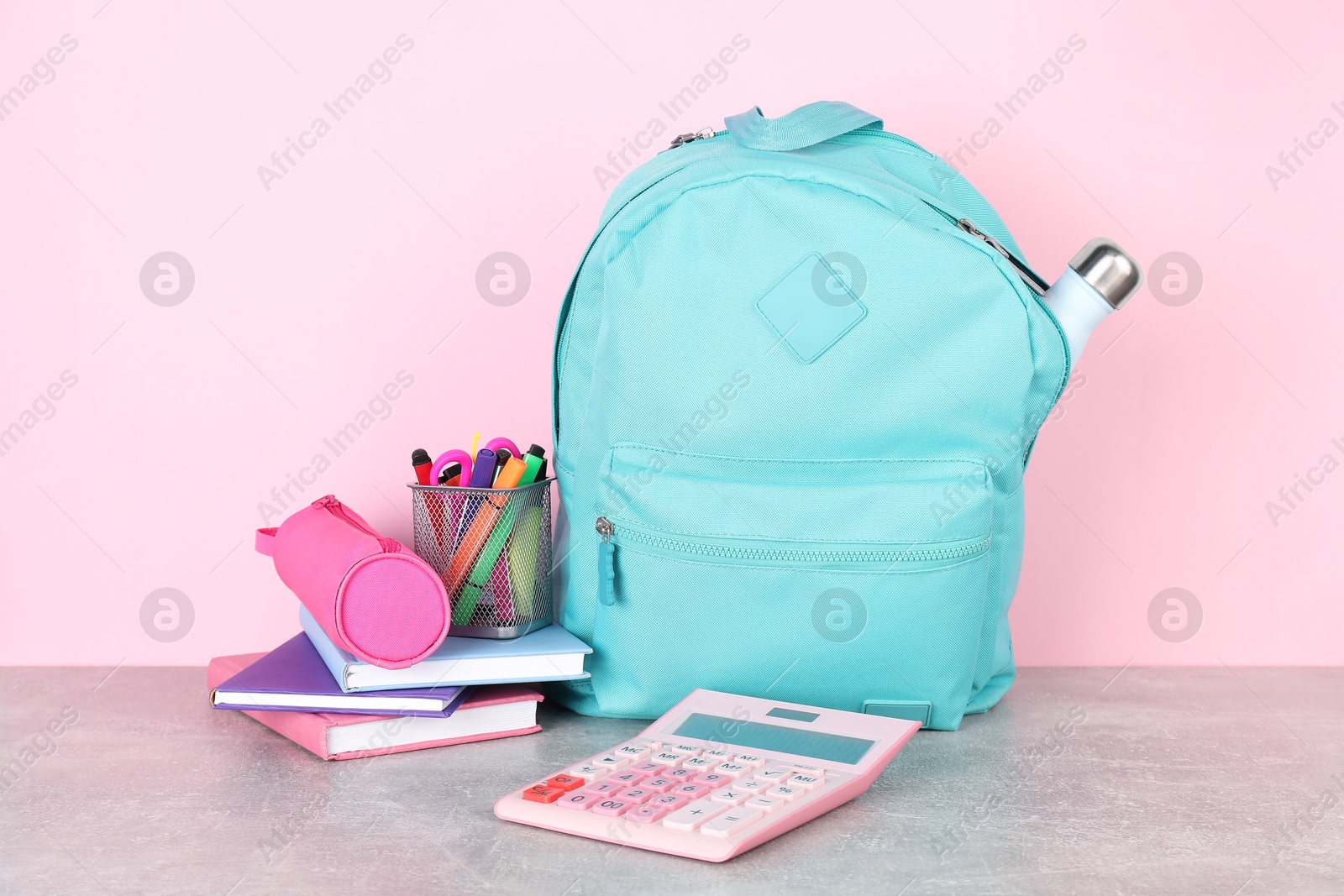 Photo of Backpack with different school stationery on light grey table against pink background