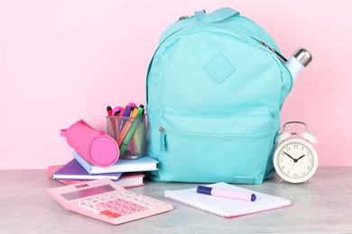 Photo of Backpack with different school stationery and alarm clock on light grey table against pink background