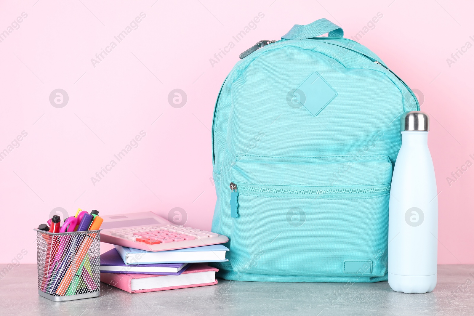 Photo of Backpack with different school stationery on light grey table against pink background